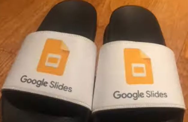 a pair of sandals of the slide variety, with white feet holsters emblazoned with the sigil of google slides oriented towards where the grippers would be; beneath the logo, the caption "Google Slides"